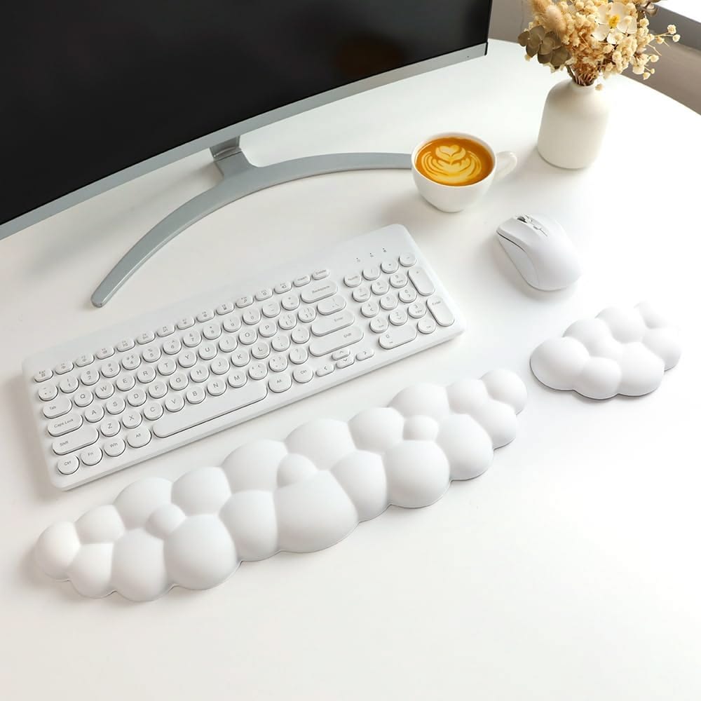 A white cloud-shaped keyboard wrist rest and matching cloud mouse pad supporting a wireless keyboard and mouse on a white desk with a computer.